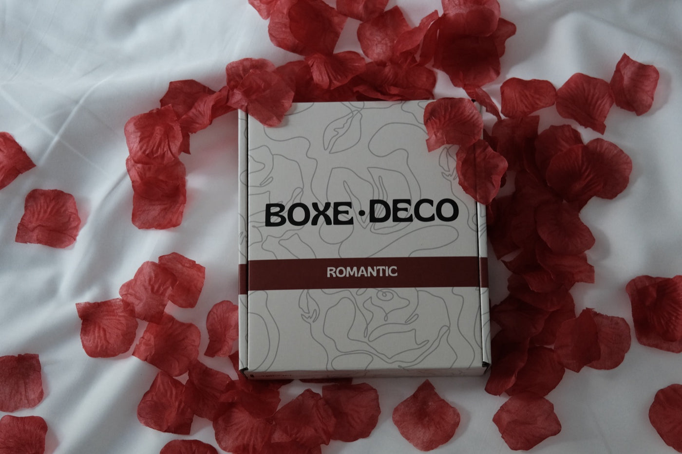 La Boxe Deco posée sur un drap blanc entourée de pétales de rose